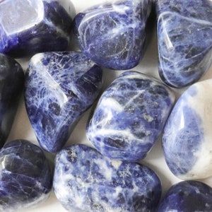 May include: A collection of tumbled blue and white sodalite stones. The stones are smooth and polished, with a variety of patterns and textures.