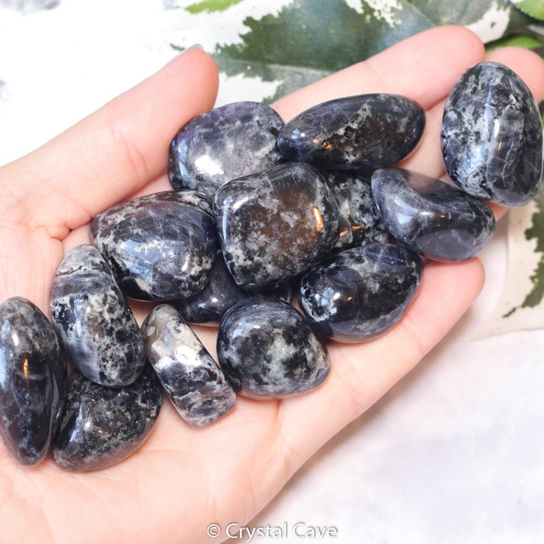 May include: A collection of tumbled blue and black spectrolite stones. The stones are smooth and polished, with a variety of shapes and sizes.