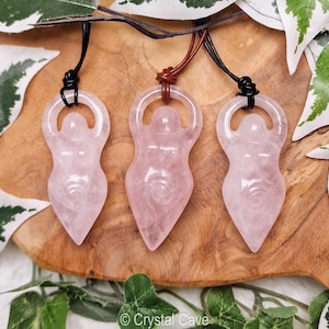 May include: Three pink rose quartz goddess pendants on black and brown leather cords. The pendants are carved in the shape of a woman with her arms raised above her head.