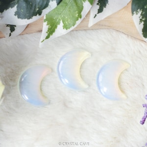 Pode incluir: Três esculturas de cristal em forma de lua crescente de opala iridescente. Os cristais são de cor azul pálido com um brilho arco-íris.