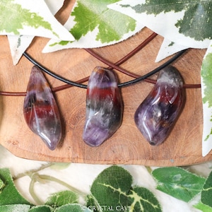 May include: Three amethyst gemstone pendants on leather cords. The amethyst stones are a deep purple with red and white inclusions. The stones are all different shapes and sizes.