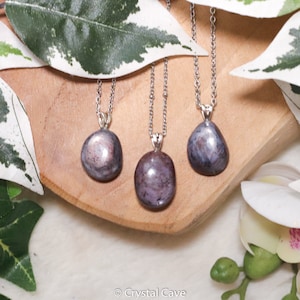 Può includere: Tre collane d'argento con ciondoli in pietra preziosa iridescente di colore viola e grigio. I ciondoli sono lisci e rotondi, e le collane sono su una superficie di legno.
