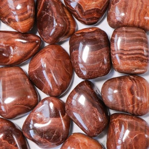 May include: A collection of tumbled red and brown tiger eye stones. The stones are smooth and polished, with a natural striated pattern.