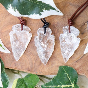 May include: Three clear quartz arrowhead pendants on brown and black leather cords. The arrowheads are polished and have a translucent appearance. The cords are tied in a knot at the top of each pendant.