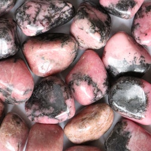May include: A collection of tumbled pink and black rhodonite stones. The stones are smooth and polished, with a variety of shapes and sizes.