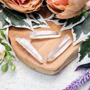 以下が含まれることがあります： 木製の表面に3つの透明な水晶ポイント。クリスタルは長く、細く、先のとがった先端を持っています。クリスタルは三角形に配置されています。