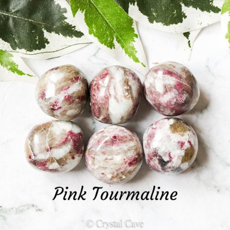 May include: Six pink tourmaline tumbled stones, each with a unique swirling pattern of pink and white. The stones are smooth and polished, and they are arranged in a circle on a white surface.