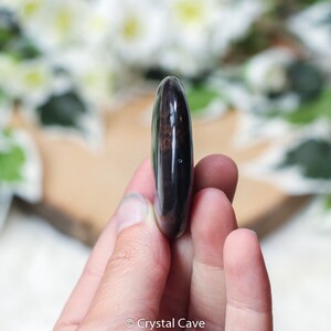 May include: A smooth, polished black obsidian palm stone with a hint of brown. The stone is oval shaped and has a glossy finish.