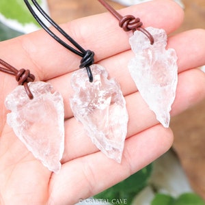 May include: Three clear quartz arrowhead pendants on brown leather cords. The arrowheads are all different sizes and shapes.