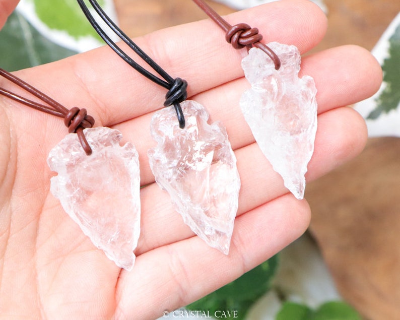 May include: Three clear quartz arrowhead pendants on brown leather cords. The arrowheads are all different sizes and shapes.