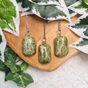Op de afbeelding: Drie groene serpentijnstenen hangers aan zilveren kettingen. De stenen zijn allemaal in verschillende vormen en maten en hebben een uniek marmerpatroon.