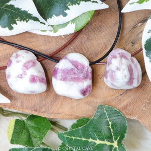 May include: Three pink and white striped gemstone pendants on a black leather cord necklace. The stones are tied to the cord with brown leather knots.