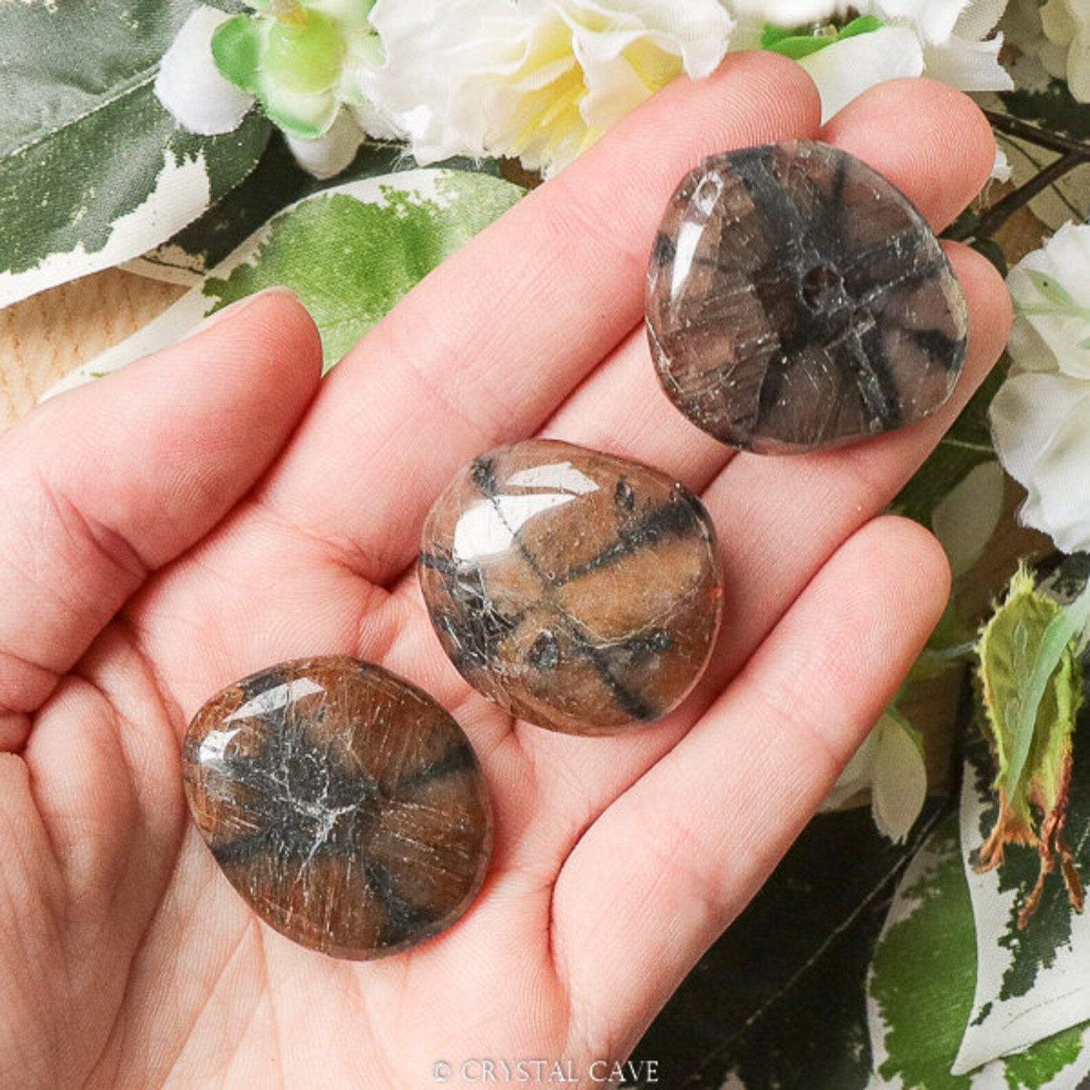 Tumbled chiastolite stones with natural cross patterns held in a hand over floral background
