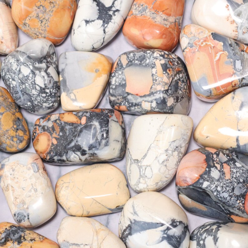 May include: A collection of tumbled ocean jasper stones in various shades of white, gray, brown, and orange. The stones have a unique, marbled pattern and are smooth to the touch.