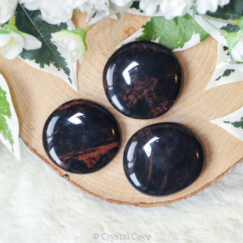 May include: Three smooth, polished black and red mahogany obsidian palm stones. The stones are round and have a glossy finish.