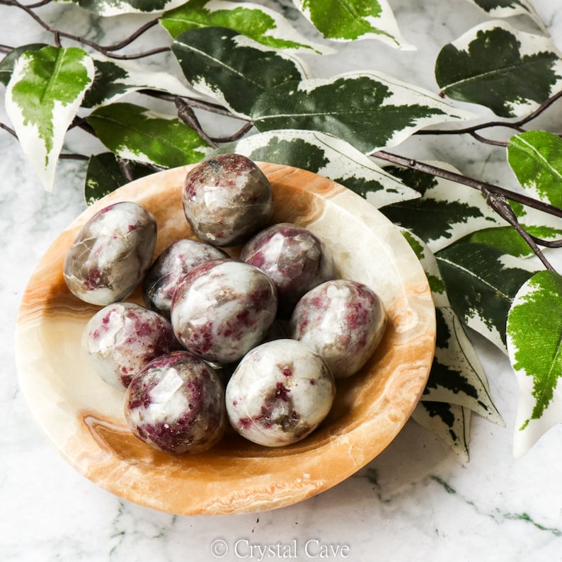 May include: A bowl of tumbled red and white jasper stones. The stones are smooth and polished, and they have a variety of shapes and sizes.
