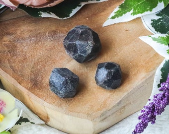 May include: Three black, faceted, gemstone crystals on a wooden surface. The crystals are in various sizes and shapes.
