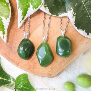 Op de afbeelding: Drie jade-stenen hangers aan zilveren kettingen. De stenen zijn in verschillende vormen en maten en allemaal in een diepe groene kleur.