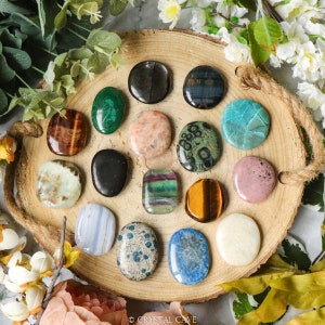 May include: A collection of 15 polished tumbled stones, each with a unique color and pattern, arranged in a circle on a wooden tray. The stones include tiger's eye, amethyst, green aventurine, and more.
