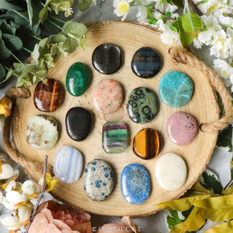 May include: A collection of 15 polished tumbled stones, each with a unique color and pattern, arranged in a circle on a wooden tray. The stones include tiger's eye, amethyst, green aventurine, and more.