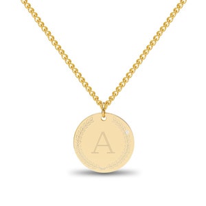 May include: A gold necklace with a round pendant featuring the letter "A" surrounded by a laurel wreath design. The pendant has a small diamond accent.