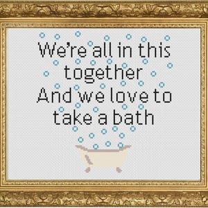 Könnte beinhalten: Kreuzstich-Kunstwerk in einem goldenen Rahmen. Das Kunstwerk zeigt den Text "We're all in this together And we love to take a bath" mit einer kleinen Badewannen-Grafik und blauen Blasen. Der Hintergrund ist weiß.