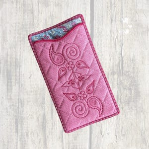 May include: A rectangular pink quilted fabric pouch featuring a stitched floral and paisley pattern on the front. The top opening reveals a contrasting interior lining with a blue, pink, and white floral print. The edges are finished with pink trim.