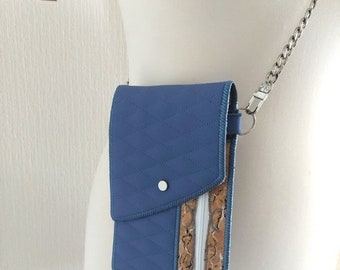 May include: A blue quilted crossbody bag with a flap closure and a silver chain strap. The bag features a decorative panel with a cork-like texture and a white vertical stripe. A small white button secures the flap.