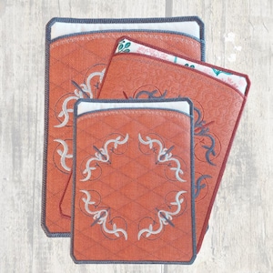 Peut inclure: Trois maniques en tissu matelassé avec un motif brodé décoratif. Les maniques sont dans des tons d'orange et de blanc.