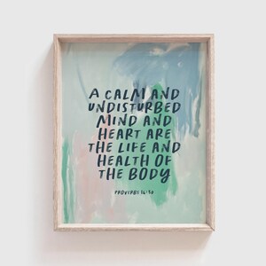 May include: Framed art print with a light wood frame. The artwork features an abstract background in shades of blue, green, and pink. The text reads: "A CALM AND UNDISTURBED MIND AND HEART ARE THE LIFE AND HEALTH OF THE BODY" from Proverbs 16:30.