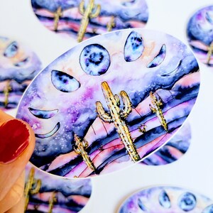 May include: Oval stickers featuring a watercolor design of a desert landscape with cacti and a night sky with moon phases. The color palette includes purple, blue, and gold.