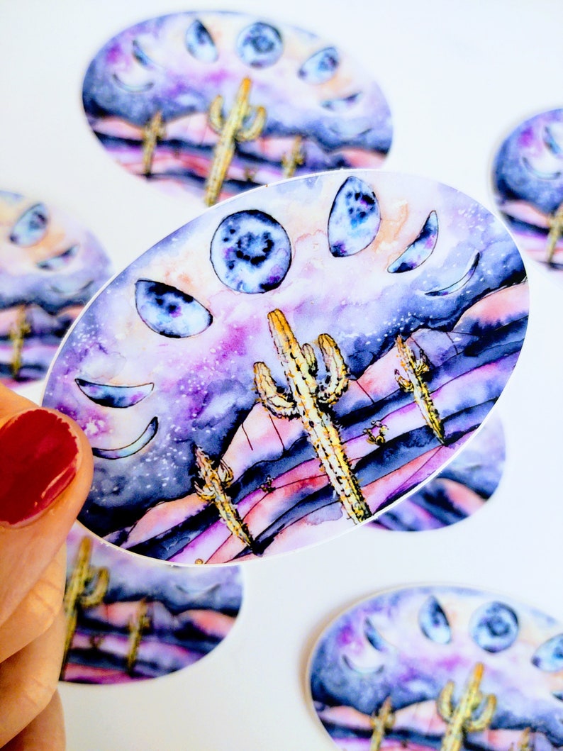 May include: Oval stickers featuring a watercolor design of a desert landscape with cacti and a night sky with moon phases. The color palette includes purple, blue, and gold.