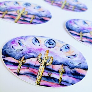 May include: Oval stickers featuring a watercolor desert scene with cacti, a starry sky, and moon phases. The color palette includes purple, pink, and yellow. The stickers are on a white background.