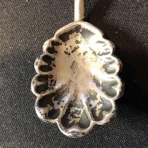 Puede incluir: Una cuchara de plata con un cuenco festoneado y un mango largo y delgado.