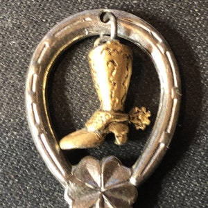 May include: A silver horseshoe charm with a gold-colored cowboy boot pendant. The boot has a spur and is hanging from the horseshoe.