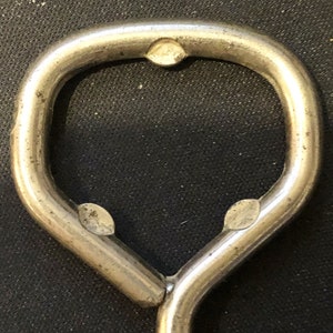 May include: Close-up of a silver bottle opener with a rounded opening. The opener has three small indentations on the top and bottom.