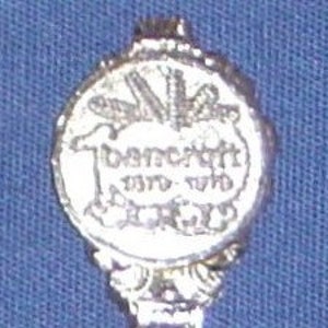 May include: Silver spoon with a round, ornate handle. The front of the spoon features a design of a feather and the words "Doctor Who" in a stylized font.