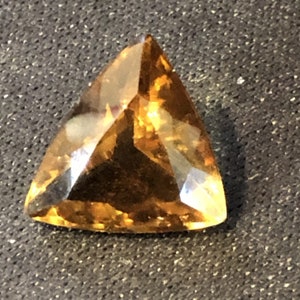 May include: A triangular, faceted gemstone with a golden-brown color.