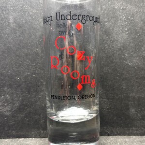 May include: A clear glass shot glass with a red and black logo that reads "Cozy Rooms" and "Pendleton, Oregon".