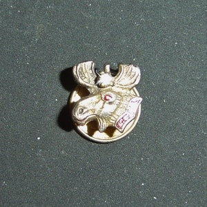 May include: A gold-colored moose head pin with red enamel accents. The moose has a white nose and a black eye.