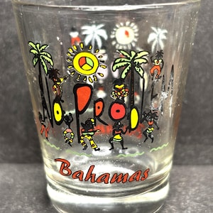 May include: Clear shot glass with a colorful design featuring palm trees, suns, and figures. The words "No Problem" are displayed vertically, with "Bahamas" in red script at the bottom. A fun souvenir.