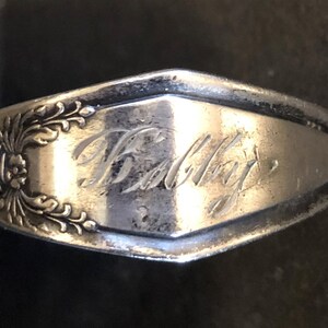 Puede incluir: Primer plano de una cuchara de plata con un diseño ornamentado y la inscripción "Halley" grabada en la parte posterior.