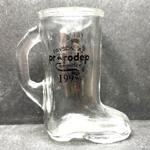 May include: A clear glass boot-shaped shot glass with a black printed design that says "Payson, AZ ProRodeo Committee 1995".