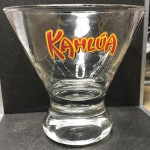 May include: A clear glass margarita glass with the words "Kahlua the everyday exotic" printed on the side. The words "Kahlua" are in red and yellow.