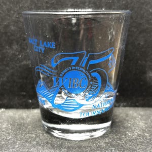 Puede incluir: Un vaso de chupito de vidrio transparente con letras azules que dicen "Salt Lake City" y "75th Annual IBC International Bowling Congress National Tournament 1994".