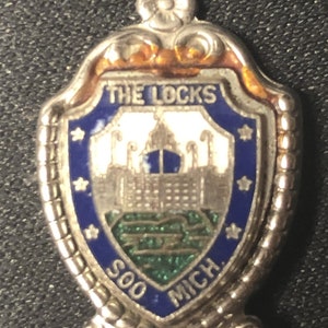 May include: Silver souvenir spoon with a blue and white enamel shield featuring a building and the text "THE LOCKS SOO MICH."