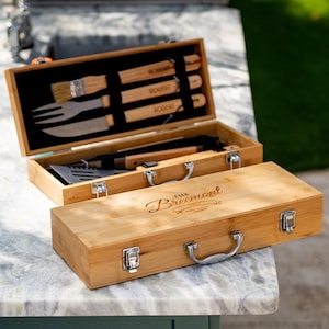 May include: A wooden box with a handle and latches. The box is engraved with "The Breemont" and has a set of grilling tools inside.