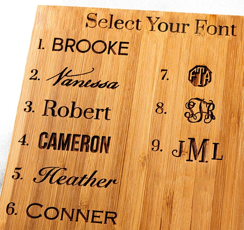 May include: A wooden board with nine different font styles to choose from for a personalized gift. The fonts include cursive, block, and monogram styles. The text on the board reads "Select Your Font".