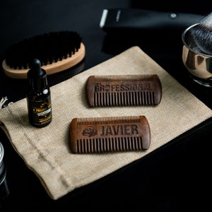 May include: Two wooden combs with engraved text. The top comb says "PROFESSIONAL" and the bottom comb says "JAVIER". The combs are on a brown burlap surface with other grooming supplies.