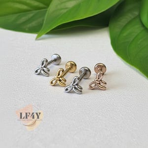 May include: Four pieces of body jewelry with a floral design. The jewelry is in silver, gold, and rose gold tones. The jewelry is on a white surface with green leaves in the background. The jewelry is from LF4Y Hand Crafted Body Jewellery.